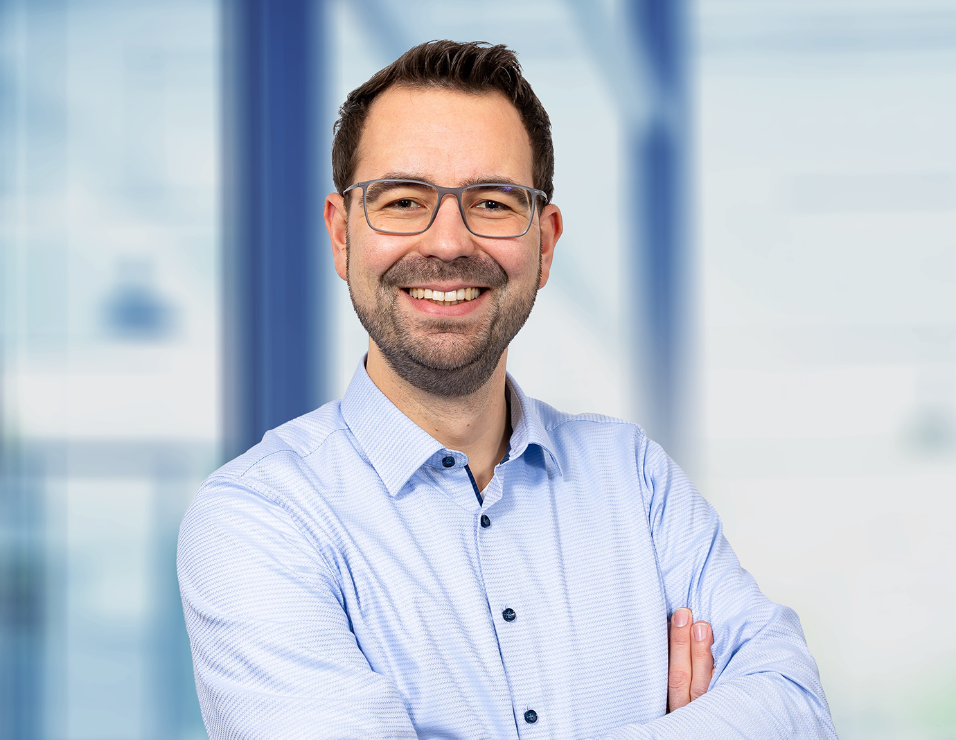 Lennart Schümann stands with his arms crossed in front of a window with a blurred background. Lennart Schümann stands with his arms crossed in front of a window with a blurred background.