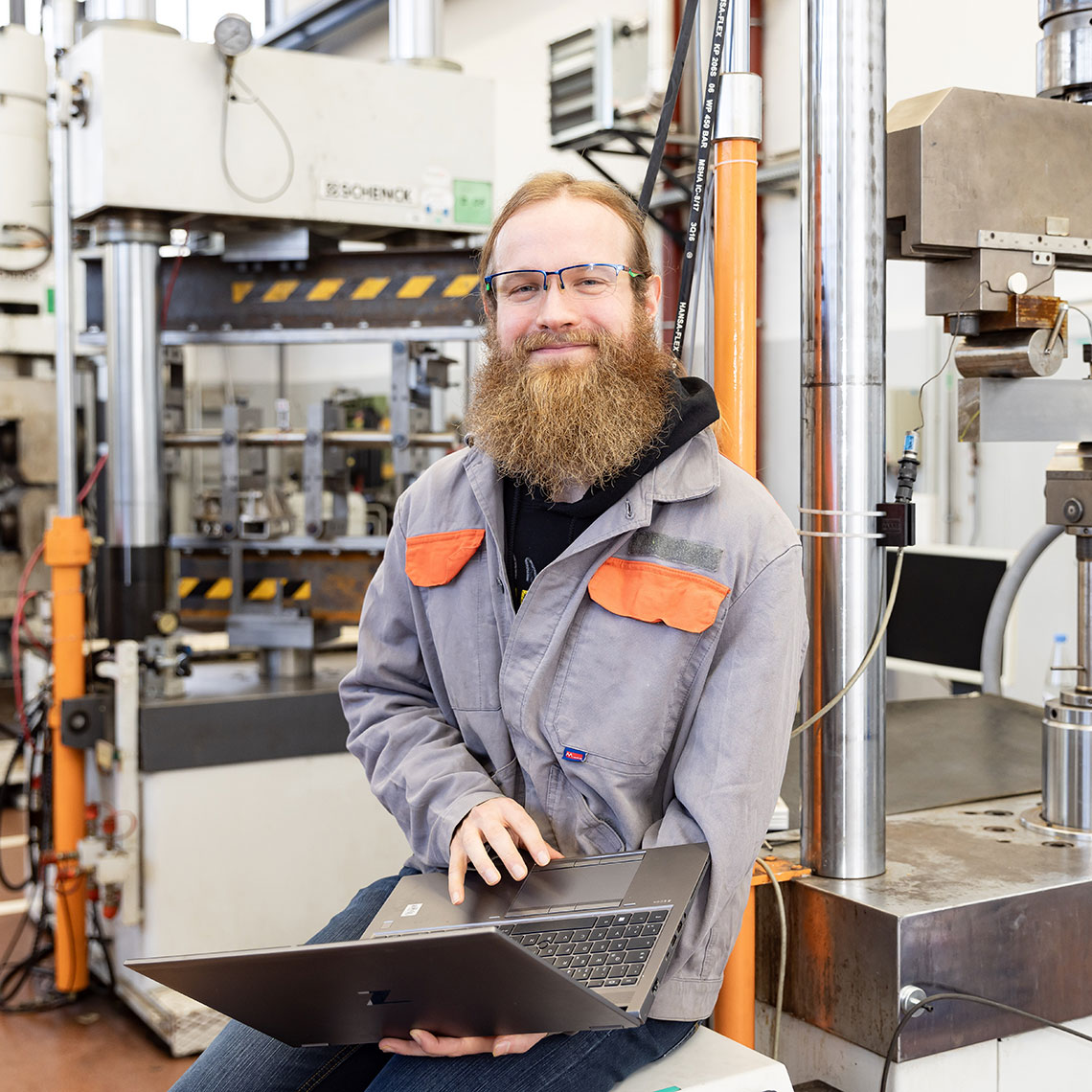Portrait photo of Fabian Spiegel, Data Scientist at Salzgitter Mannesmann Forschung GmbH. He wears grey workwear and holds an open laptop in front of him. In the background, an industrial production facility is visible. Portrait photo of Fabian Spiegel, Data Scientist at Salzgitter Mannesmann Forschung GmbH. He wears grey workwear and holds an open laptop in front of him. In the background, an industrial production facility is visible.
