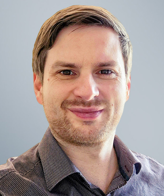 Portrait photo of Lars Schermann, microstructure analysis expert at Salzgitter Mannesmann Forschung GmbH. He wears a checked shirt and looks friendly into the camera. In the background, a microscopic image of a steel structure is visible. Portrait photo of Lars Schermann, microstructure analysis expert at Salzgitter Mannesmann Forschung GmbH. He wears a checked shirt and looks friendly into the camera. In the background, a microscopic image of a steel structure is visible.