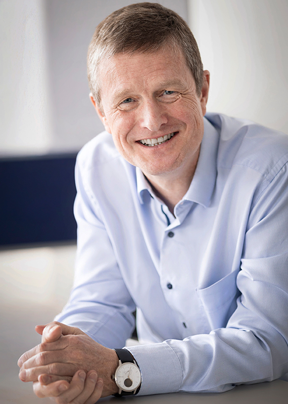 Kai Acker, CEO der KHS Gruppe, sitzt mit gefalteten Händen an einem Tisch und lächelt in die Kamera.