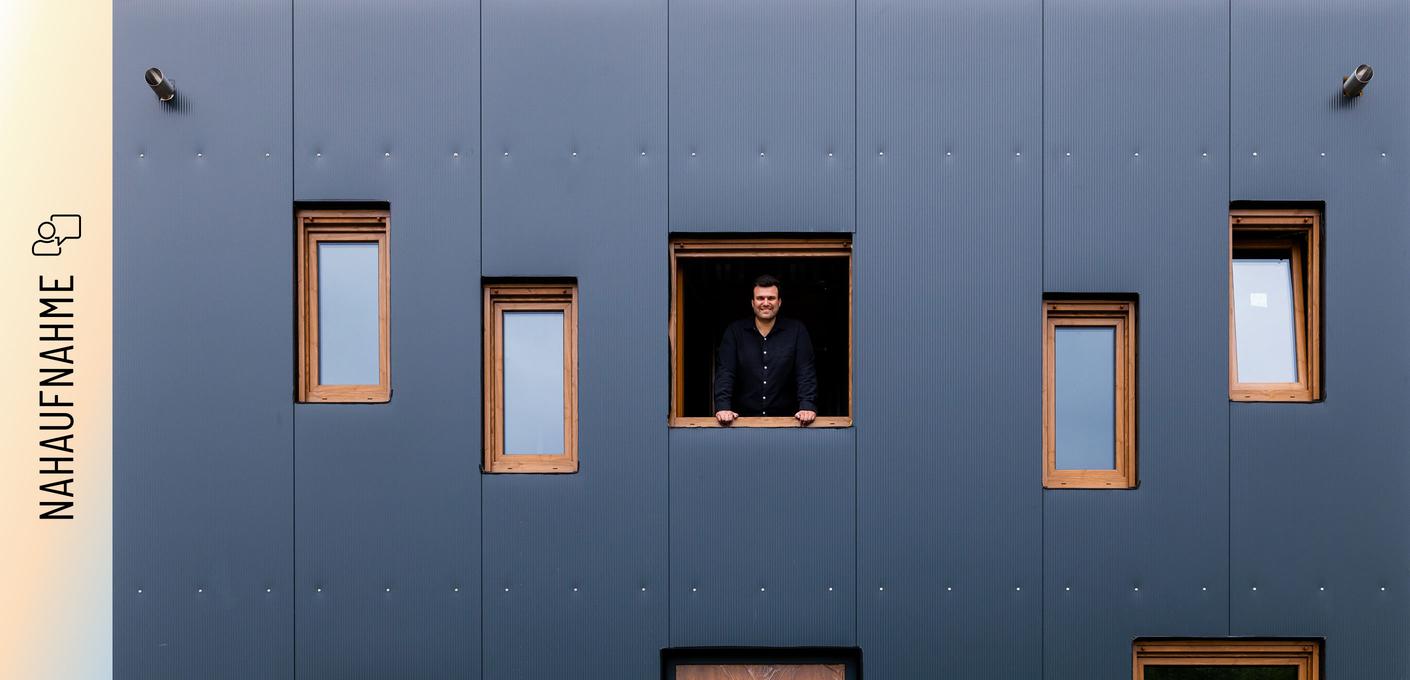 Christoph Jenner schaut aus einem Fenster der anthrazitfarbenen Stahlfassade seines Green Steel Home .