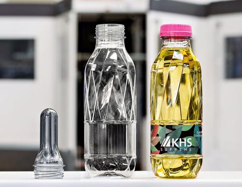 Ein PET-Rohling, eine daraus geformte transparente PET-Flasche und eine befüllte, beschichtete und etikettierte Flasche zeigen die Entwicklungsschritte vom Rohling zum fertigen Produkt.