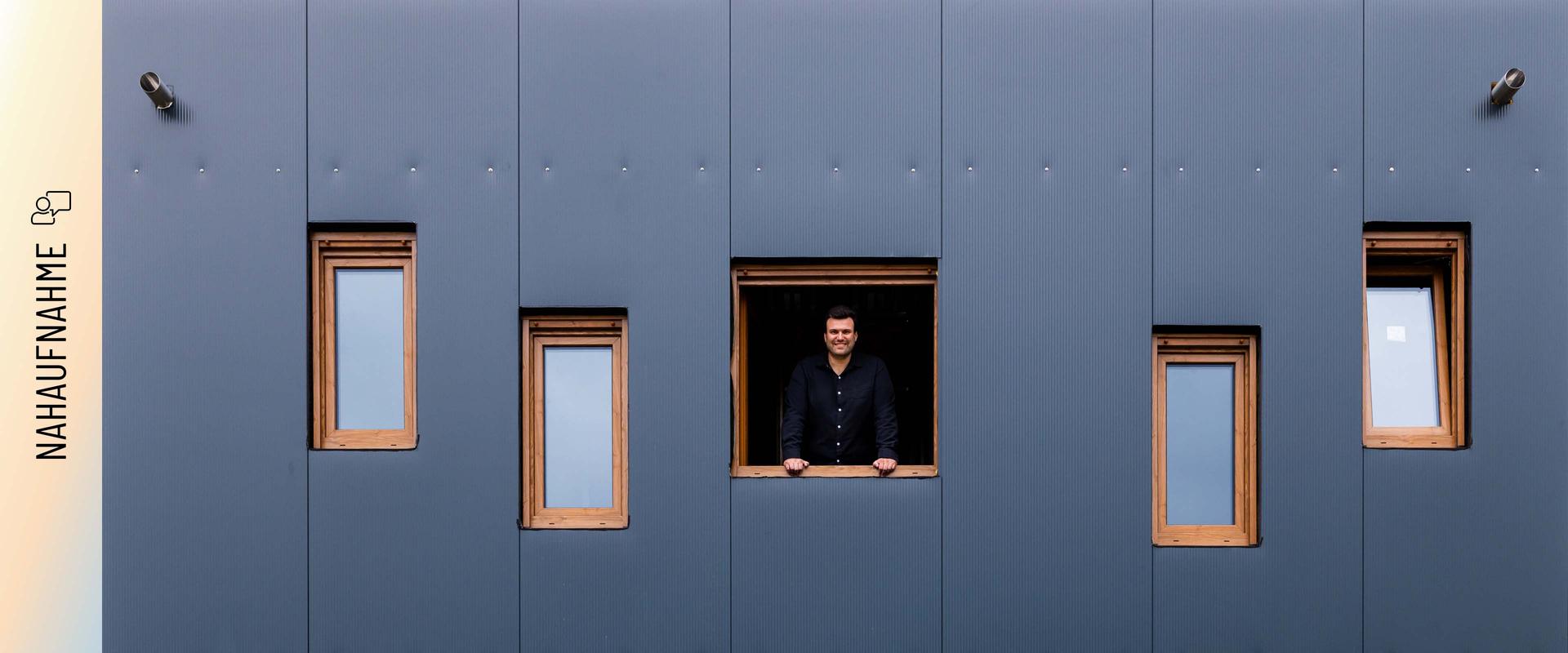 Christoph Jenner schaut aus einem Fenster der anthrazitfarbenen Stahlfassade seines Green Steel Home .