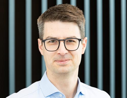 Helge Langheim in a light blue shirt in front of a background with vertical, grey slats.