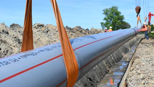H2Ready Rohr wird in einen Graben abgesenkt Das H2Ready Rohr wird mit Hilfe von Hebebändern und Kränen in einen offenen Graben auf einer Baustelle abgesenkt.
