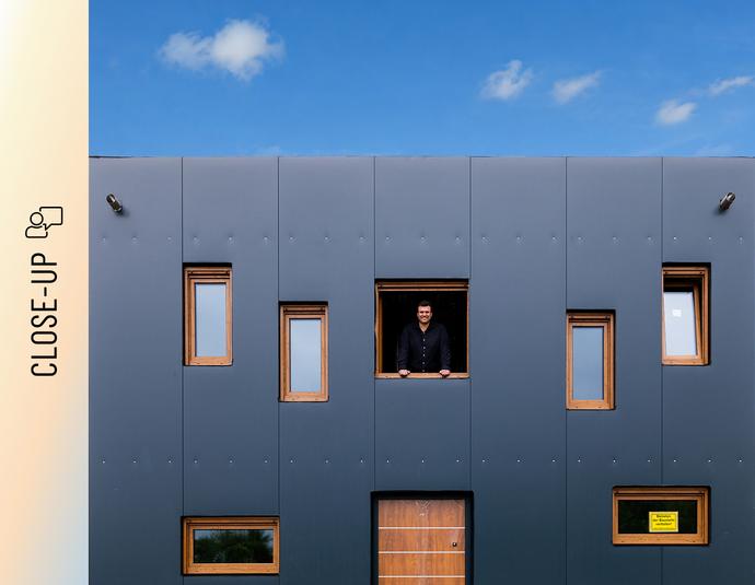 Christoph Jenner schaut aus einem Fenster der anthrazitfarbenen Stahlfassade seines Green Steel Home .