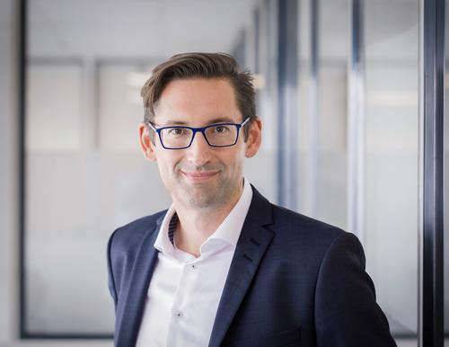 Dr. Joachim Konrad, Head of Line Solutions der KHS Gruppe, trägt eine Brille und einen dunklen Anzug und blickt lächelnd in die Kamera.