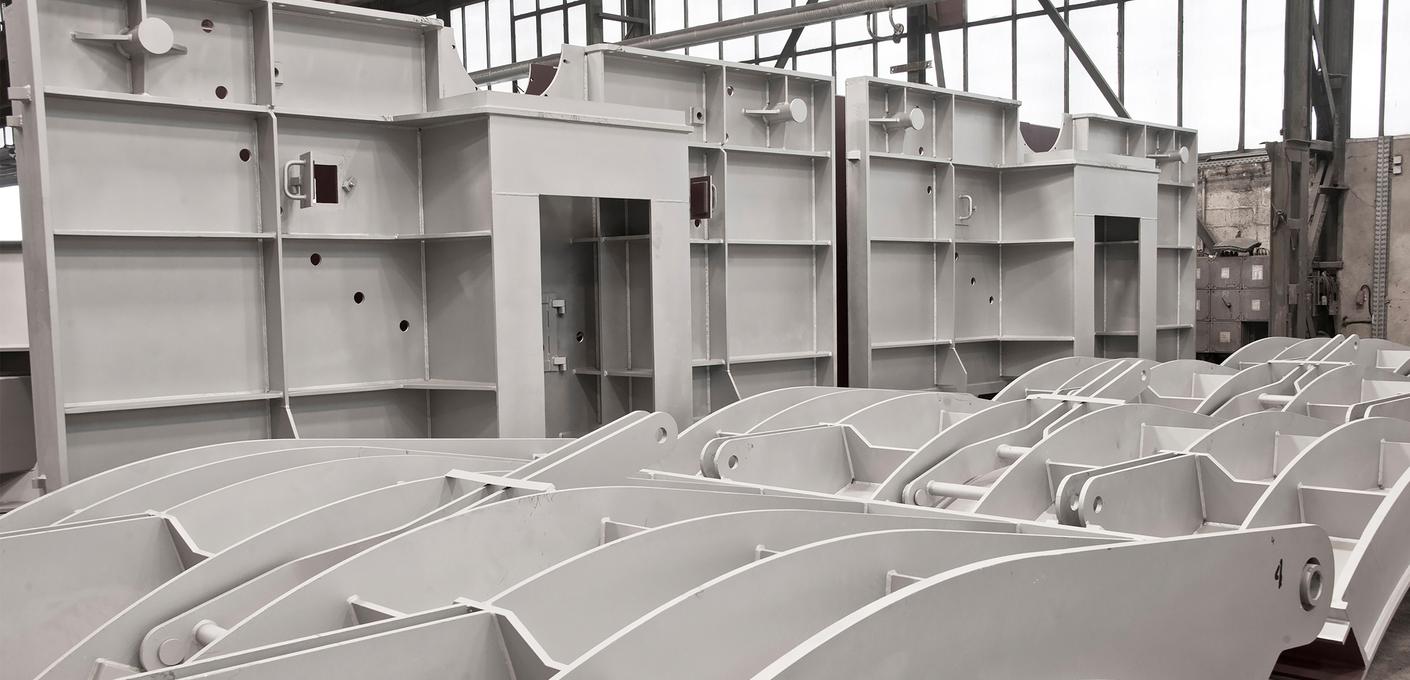 Rows of grey modular steel components with curved shapes in a production hall, showing defense components in manufacturing. Rows of grey modular steel components with curved shapes in a production hall, showing defense components in manufacturing.