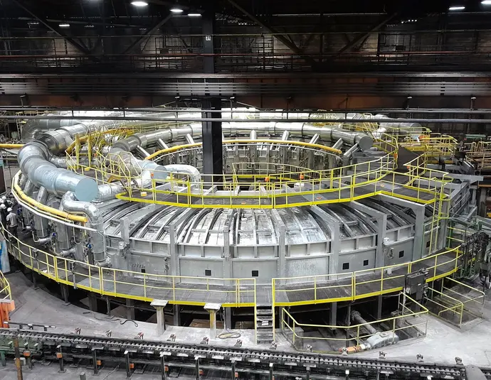 A large circular rotary hearth furnace inside the Mannesmannröhren-Werk Zeithain plant, surrounded by yellow walkways and pipework.