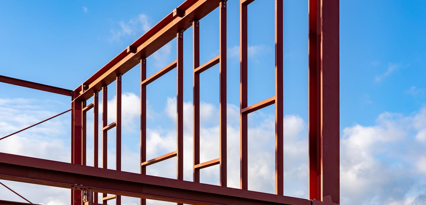 Stahlskelettkonstruktion eines Wohngebäudes in der Bauphase Rote Stahlskelettkonstruktion eines Wohngebäudes in der Bauphase vor blauem Himmel mit weißen Wolken – zeigt die tragende Struktur aus Stahlprofilen
