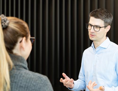 Helge Langheim in an interview situation in front of a wall with vertical, dark slats.