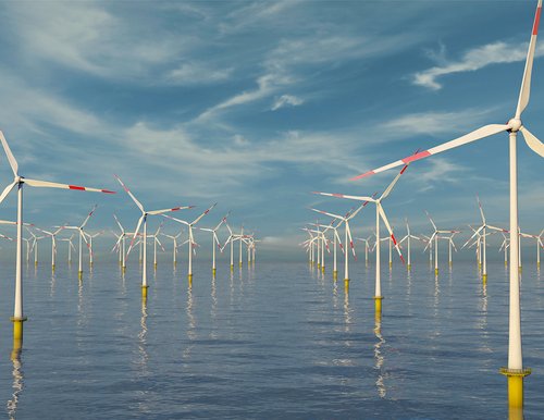 Offshore-Windkraftanlagen Blick über ein ruhiges Meer auf eine Reihe von Offshore-Windkraftanlagen, die sich bis zum Horizont erstrecken. Der Himmel ist leicht bewölkt.