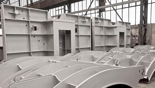 Verteidigungskomponenten in der Fertigung Reihen von grauen modularen Stahlbauteilen mit geschwungenen Formen in einer Produktionshalle, zeigt Verteidigungskomponenten in der Fertigung.