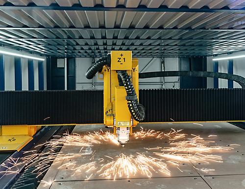 Yellow industrial robot with laser system processing steel sheet parts in a production hall. Yellow industrial robot with laser system processing steel sheet parts in a production hall.