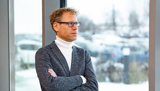 Friedrich Ellebrecht im Porträt Friedrich Ellebrecht steht mit verschränkten Armen im Anzug und weißem Rollkragenpullover vor einem Fenster.