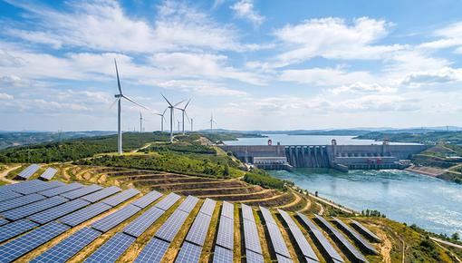 Montage mit Darstellung von Solar- und Windkraftanlagen an einem Wasserkraftwerk. Montage im Stil einer Luftaufnahme. Zeigt eine Landschaft mit großflächigen Solarmodulen im Vordergrund, mehreren Windkraftanlagen auf bewaldeten Hügeln und einem Wasserkraftwerk mit Staudamm und Stausee im Hintergrund.
